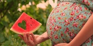 slice of watermelon in the hand of a pregnant woman
